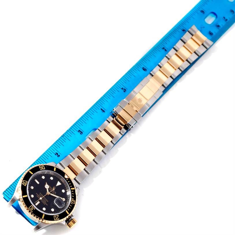 The image shows a Rolex Submariner 16613 Men's Steel and Gold (two tone) Black Dial 16613 Men's Steel and Gold (two tone) Black Dial watch laid flat alongside a ruler, highlighting its bracelet and face from a top-down view.