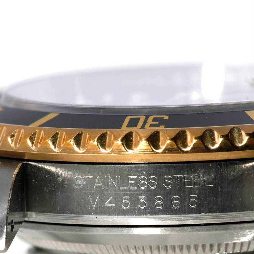The image shows a close-up side view of a Rolex Submariner 16613 Men's Steel and Gold (two tone) Black Dial 16613 Men's Steel and Gold (two tone) Black Dial's bezel, crystal, and stainless steel case with visible engraving.