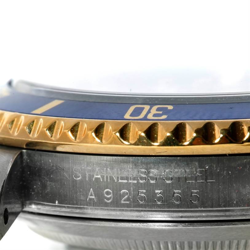 The image shows a close-up angle of the Rolex Submariner 16613 Men's Steel and Gold (two tone) Grey Dial 16613 Men's Steel and Gold (two tone) Grey Dial's bezel, case, and engraved serial number.