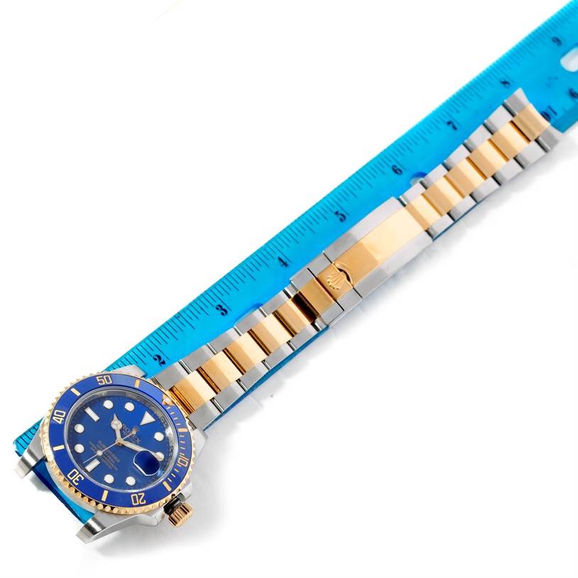 The image shows a Rolex Submariner 116613 Men's Steel and Gold (two tone) Blue Dial 116613 Men's Steel and Gold (two tone) Blue Dial watch placed next to a blue ruler, highlighting the watch face and bracelet.