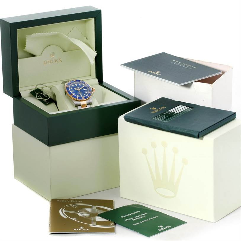 The image shows a Rolex Submariner 116613 Men's Steel and Gold (two tone) Blue Dial 116613 Men's Steel and Gold (two tone) Blue Dial watch displayed in an open box, with additional accessories and manuals nearby.