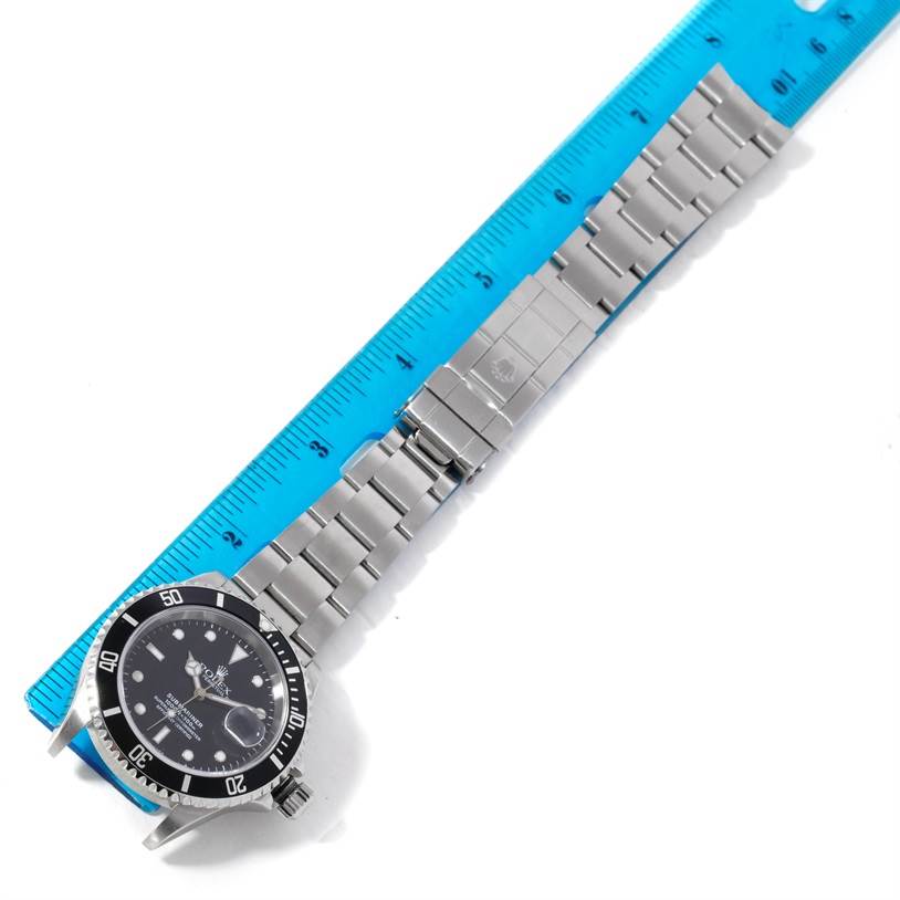 The Rolex Submariner 16610 Men
s Stainless Steel Black Dial 16610 Men
s Stainless Steel Black Dial watch is displayed lying flat with its face, bezel, and stainless steel bracelet visible, measured against a ruler.