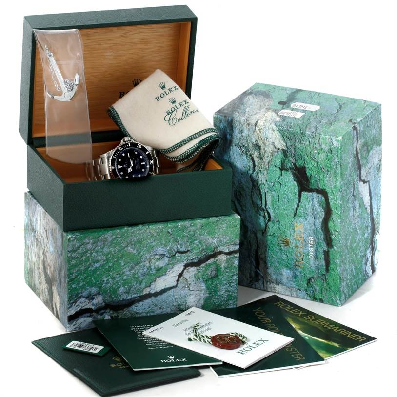 The image shows a Rolex Submariner 16610 Men
s Stainless Steel Black Dial 16610 Men
s Stainless Steel Black Dial watch in its original box with manuals, tags, and a cleaning cloth.