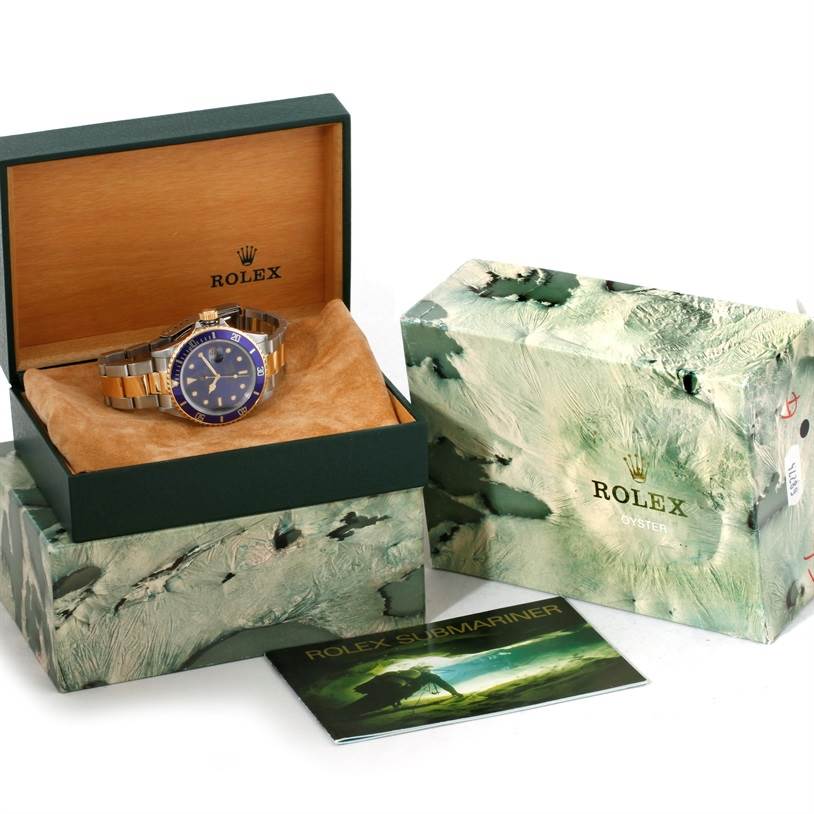 The image shows a Rolex Submariner 16803 Men's Steel and Gold (two tone) Blue Dial 16803 Men's Steel and Gold (two tone) Blue Dial watch with its open box, closed box, and a booklet.