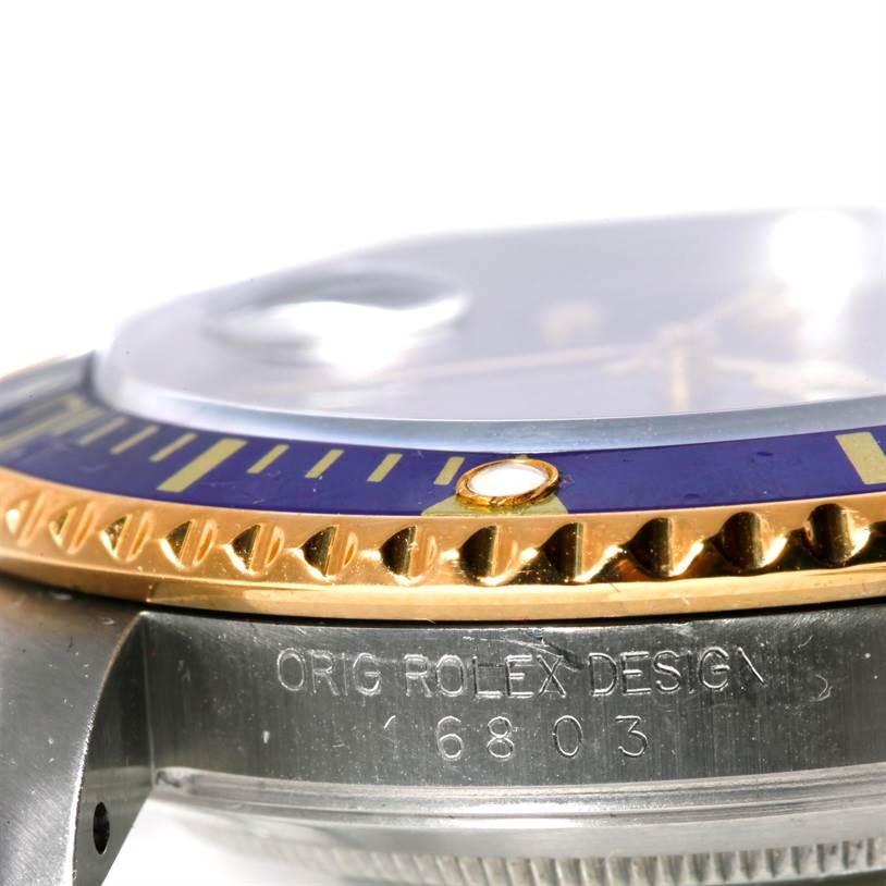 The image shows a side view of the Rolex Submariner 16803 Men's Steel and Gold (two tone) Blue Dial 16803 Men's Steel and Gold (two tone) Blue Dial bezel, crystal, and part of the case, including the "ORIG ROLEX DESIGN 16803" text.