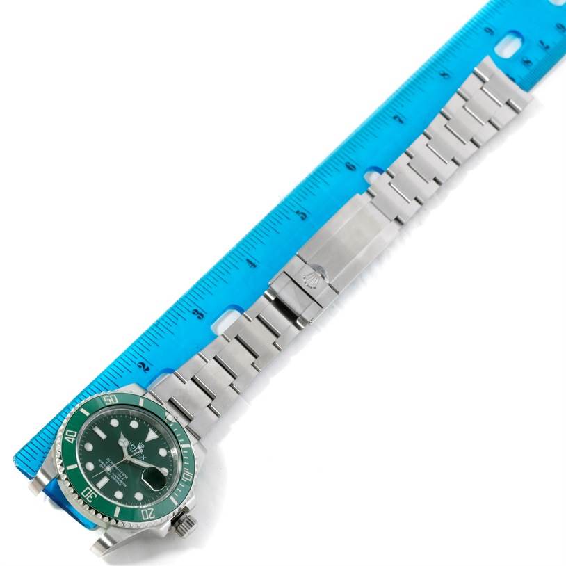 The image shows a Rolex Submariner 116610LV Men's Stainless Steel Green Dial 116610LV Men's Stainless Steel Green Dial watch laid flat alongside a blue ruler, highlighting its bracelet and green dial.