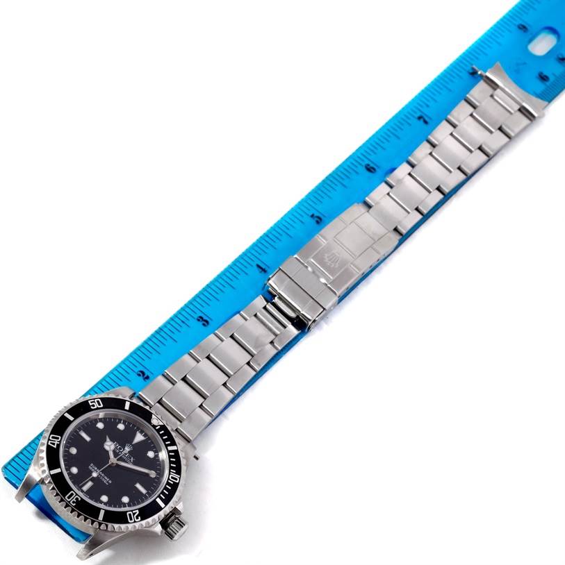 The image shows the entire Rolex Submariner 14060 Men
s Stainless Steel Black Dial 14060 Men
s Stainless Steel Black Dial watch, including the face, bezel, and metallic bracelet, positioned next to a ruler.