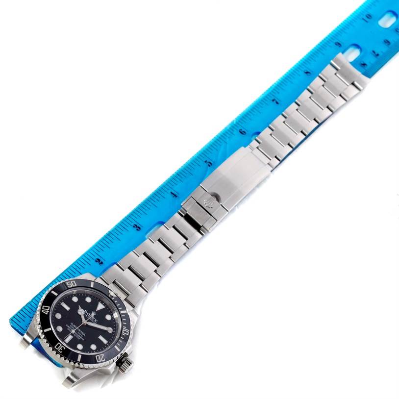 The image shows a Rolex Submariner 114060 Men
s Stainless Steel Black Dial 114060 Men
s Stainless Steel Black Dial watch laid flat with its bracelet extended alongside a blue ruler for measurement.