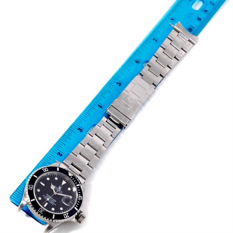 This image shows a top view of a Rolex Submariner 16610 Men
s Stainless Steel Black Dial 16610 Men
s Stainless Steel Black Dial watch including its face and stainless steel bracelet next to a blue ruler.