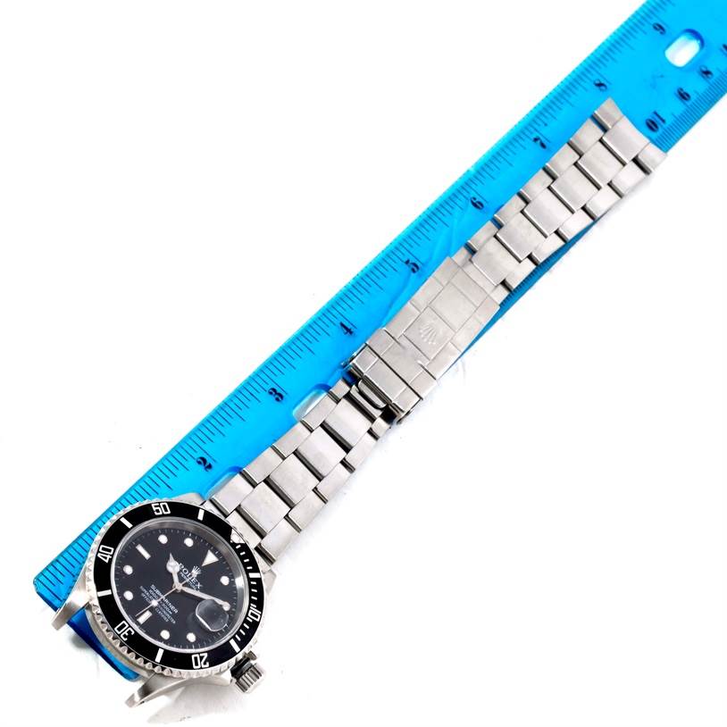 The Rolex Submariner 16610 Men
s Stainless Steel Black Dial 16610 Men
s Stainless Steel Black Dial watch is shown from a top-down angle, featuring the dial, bezel, and full bracelet alongside a ruler.