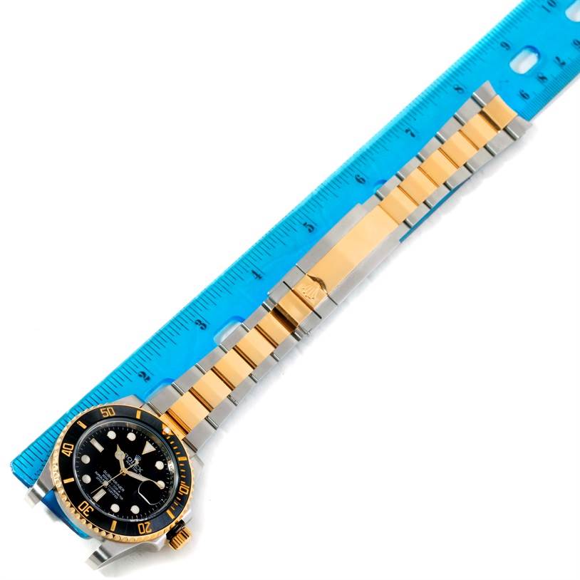 The Rolex Submariner 116613 Men's Steel and Gold (two tone) Black Dial 116613 Men's Steel and Gold (two tone) Black Dial watch is shown at a top-down angle with its face and bracelet next to a blue ruler.