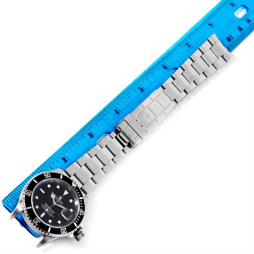 The image shows a Rolex Submariner 16610 Men
s Stainless Steel Black Dial 16610 Men
s Stainless Steel Black Dial watch laid flat with a blue ruler for measurement, displaying the face and entire metal bracelet.