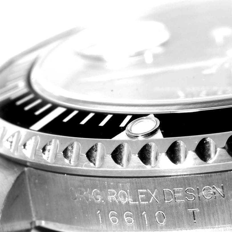 This close-up shot of the Rolex Submariner 16610 Men
s Stainless Steel Black Dial 16610 Men
s Stainless Steel Black Dial shows the bezel, part of the dial, and "ORIG. ROLEX DESIGN 16610 T" engraving.