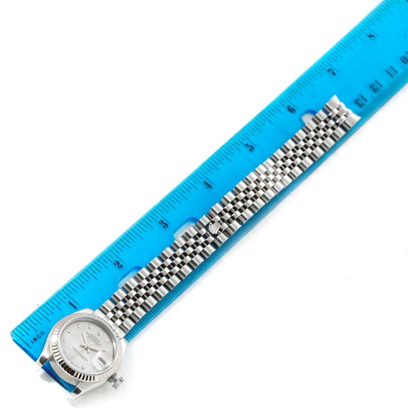 The image shows a Rolex Datejust 179174 Women's Stainless Steel Mother of Pearl Dial 179174 Women's Stainless Steel Mother of Pearl Dial watch angled horizontally alongside a blue ruler, highlighting the watch's face and bracelet.