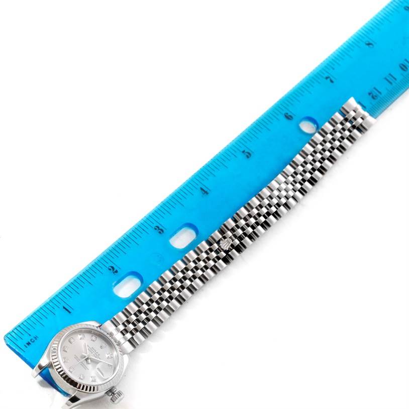 The image shows a top-down view of a Rolex Datejust 179174 Women
s Stainless Steel Silver Dial 179174 Women
s Stainless Steel Silver Dial watch with a blue measuring scale alongside its metal bracelet.