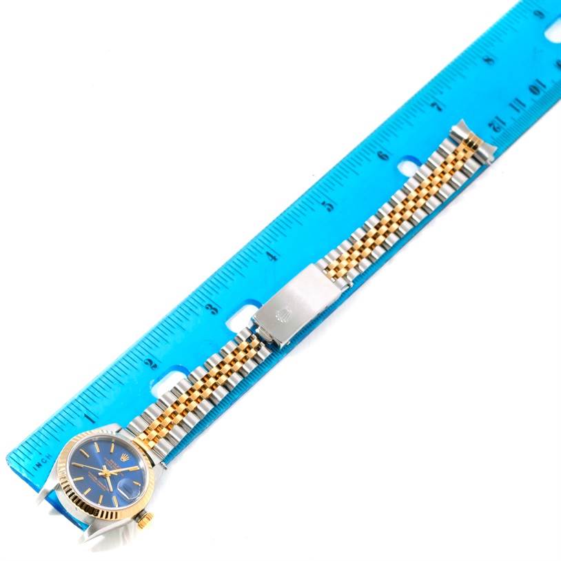 The image shows a Rolex Datejust 79173 Women's Stainless Steel Blue Dial 79173 Women's Stainless Steel Blue Dial watch laid flat next to a blue ruler, displaying its band and part of the face.