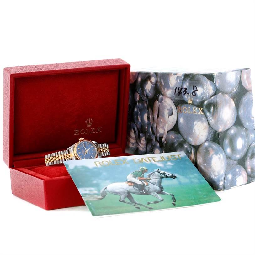 The image shows a Rolex Datejust 79173 Women's Stainless Steel Blue Dial 79173 Women's Stainless Steel Blue Dial watch partially exposed from its red case, alongside its outer box and an illustrated manual.