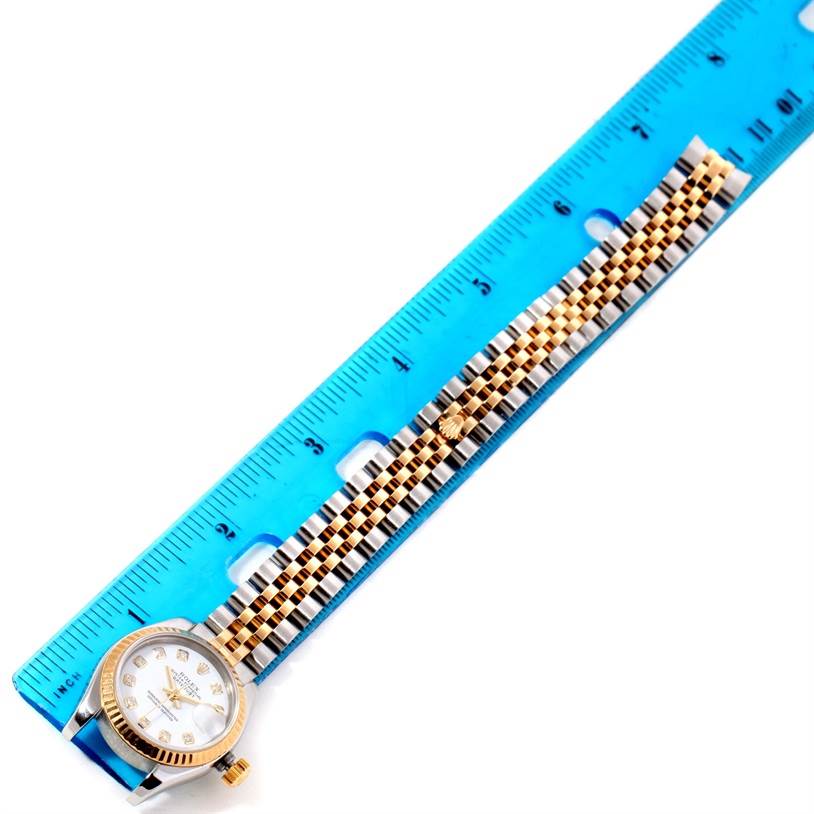 The Rolex Datejust 179173 Women's Steel and Gold (two tone) White Dial 179173 Women's Steel and Gold (two tone) White Dial watch is shown lying flat next to a ruler, displaying the face and bracelet.