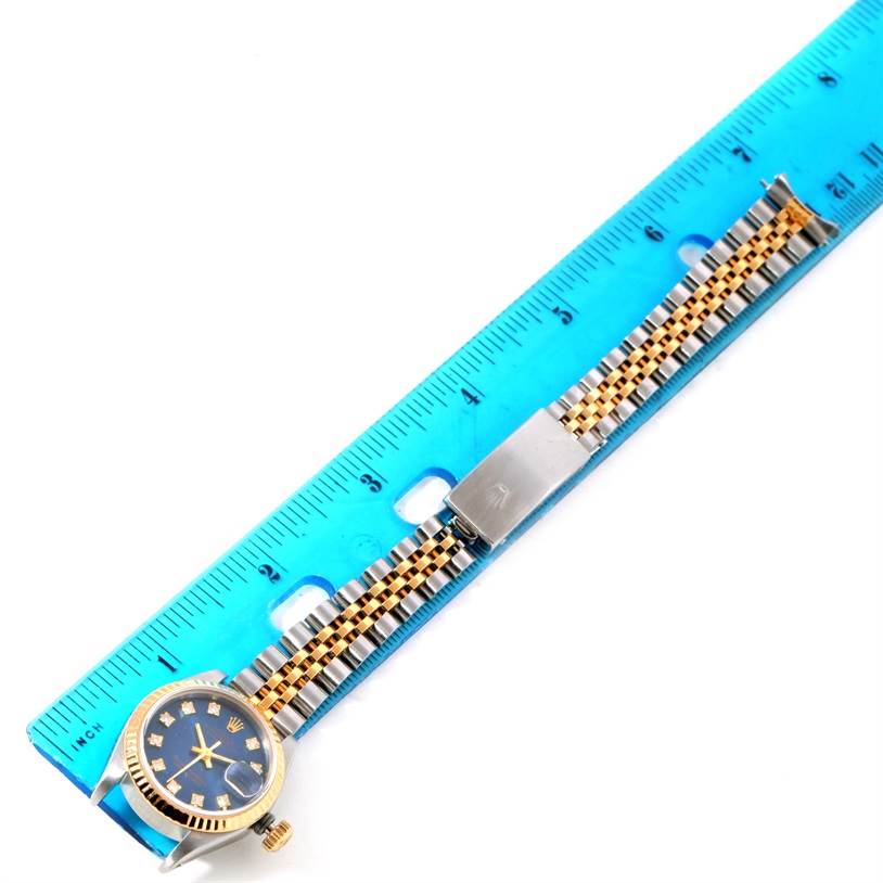 The Rolex Datejust 69173 Women
s Stainless Steel Blue Dial 69173 Women
s Stainless Steel Blue Dial watch, shown from a top view, features a blue face, bezel, and metal band next to a blue ruler for scale.