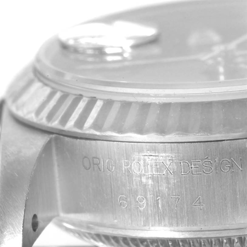 The image displays a close-up side view of a Rolex Datejust 69174 Women
s Stainless Steel Black Dial 69174 Women
s Stainless Steel Black Dial watch case, showing the model number and "ORIG ROLEX DESIGN" engraving.