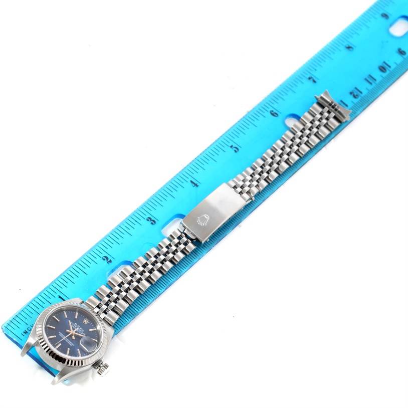 The image shows a top view of a Rolex Datejust 79174 Women
s Stainless Steel Blue Dial 79174 Women
s Stainless Steel Blue Dial watch with a jubilee bracelet alongside a blue ruler for scale.