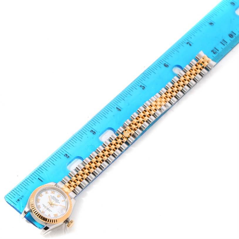 The image shows a Rolex Datejust 179173 Women's Steel and Gold (two tone) White Dial 179173 Women's Steel and Gold (two tone) White Dial watch placed adjacent to a blue ruler, displaying the dial, bezel, and two-tone bracelet.