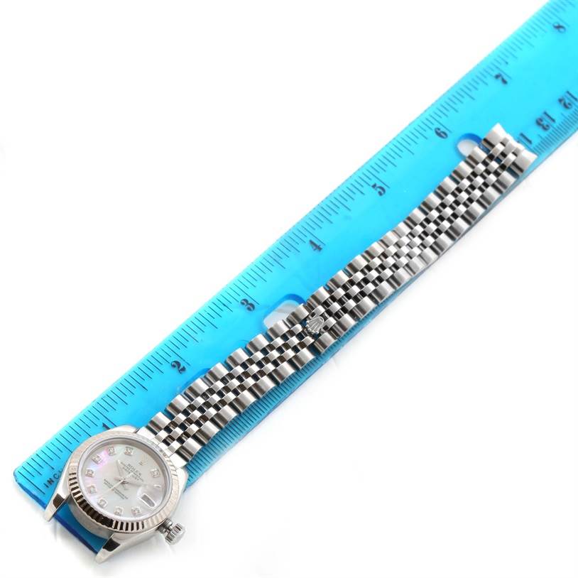 The Rolex Datejust 179174 Women
s Stainless Steel Mother of Pearl Dial 179174 Women
s Stainless Steel Mother of Pearl Dial watch is shown from a top-down angle with its case, dial, and bracelet visible next to a blue ruler.