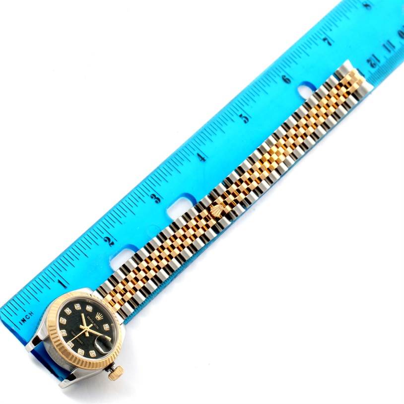 The image shows a Rolex Datejust 179173 Women's Steel and Gold (two tone) Black Dial 179173 Women's Steel and Gold (two tone) Black Dial watch laid beside a ruler, displaying the watch face and the full length of the bracelet.