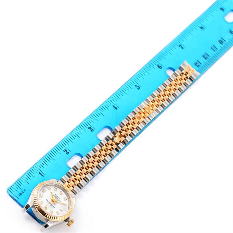 The Rolex Datejust 179173 Women's Steel and Gold (two tone) Black Dial 179173 Women's Steel and Gold (two tone) Black Dial watch is shown from the front, laying flat alongside a ruler, highlighting its face and bracelet.