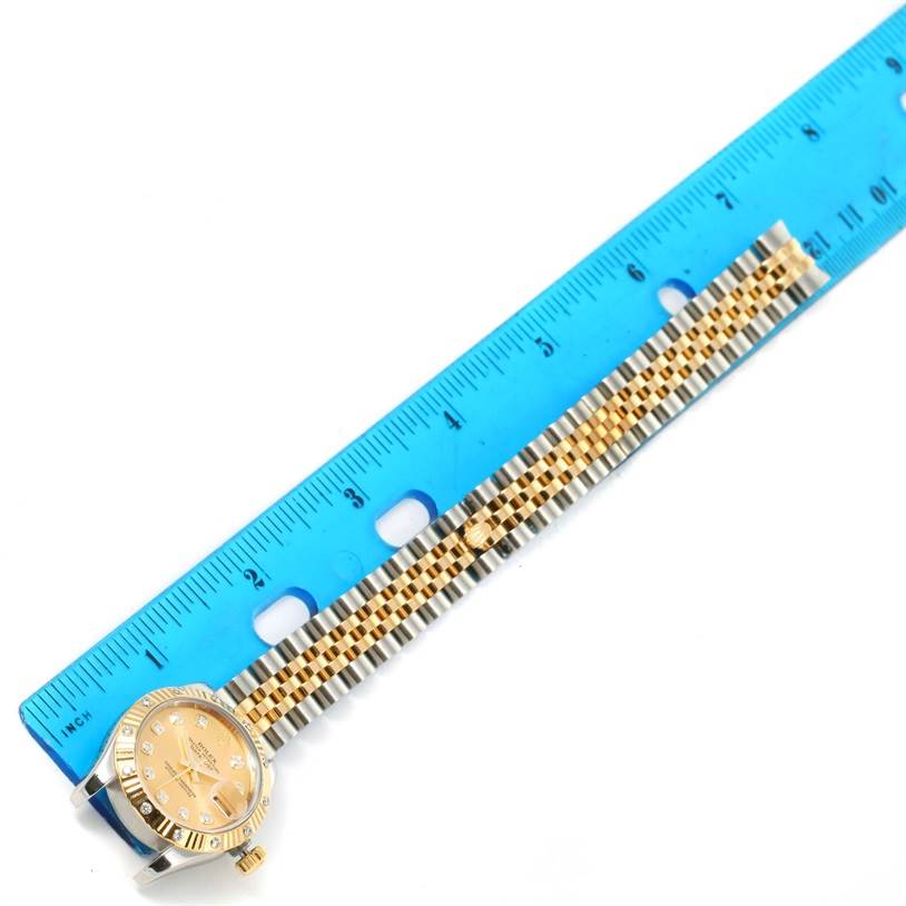 This image shows a Rolex Datejust 179313 Women
s Stainless Steel Champagne Dial 179313 Women
s Stainless Steel Champagne Dial watch placed next to a blue ruler, displaying its gold and silver bracelet and face.