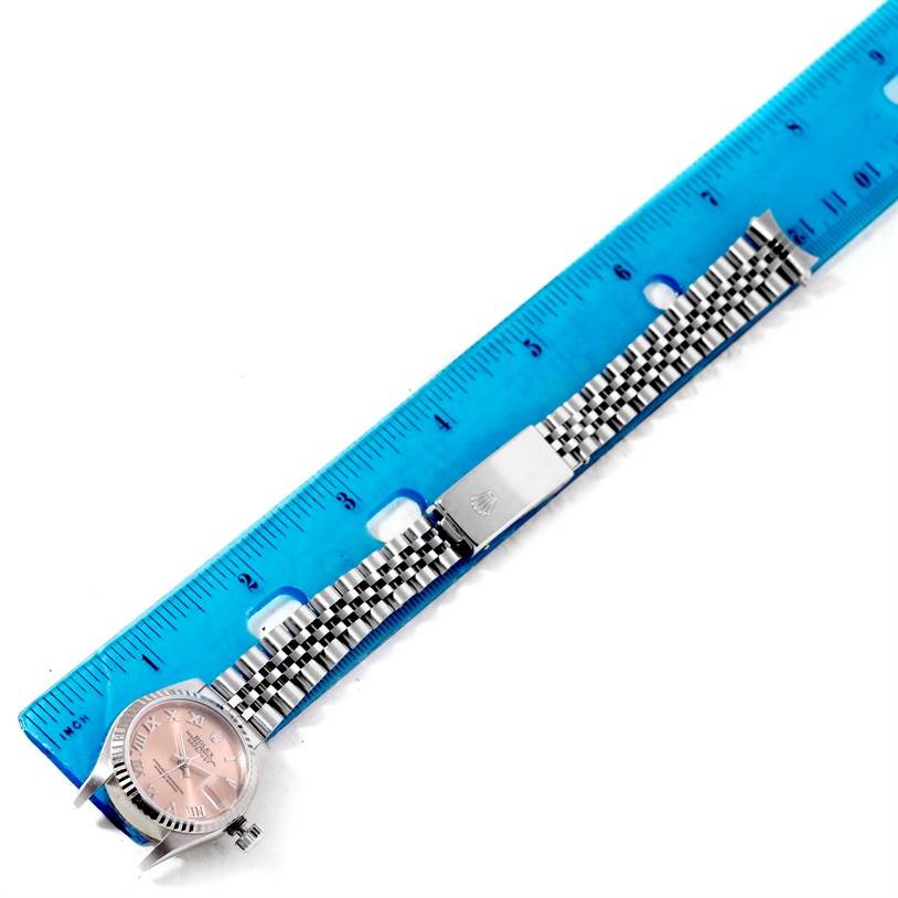 The image shows a Rolex Datejust 79174 Women's Stainless Steel Pink Dial 79174 Women's Stainless Steel Pink Dial watch placed next to a blue ruler, highlighting the watch's face, case, and jubilee bracelet.