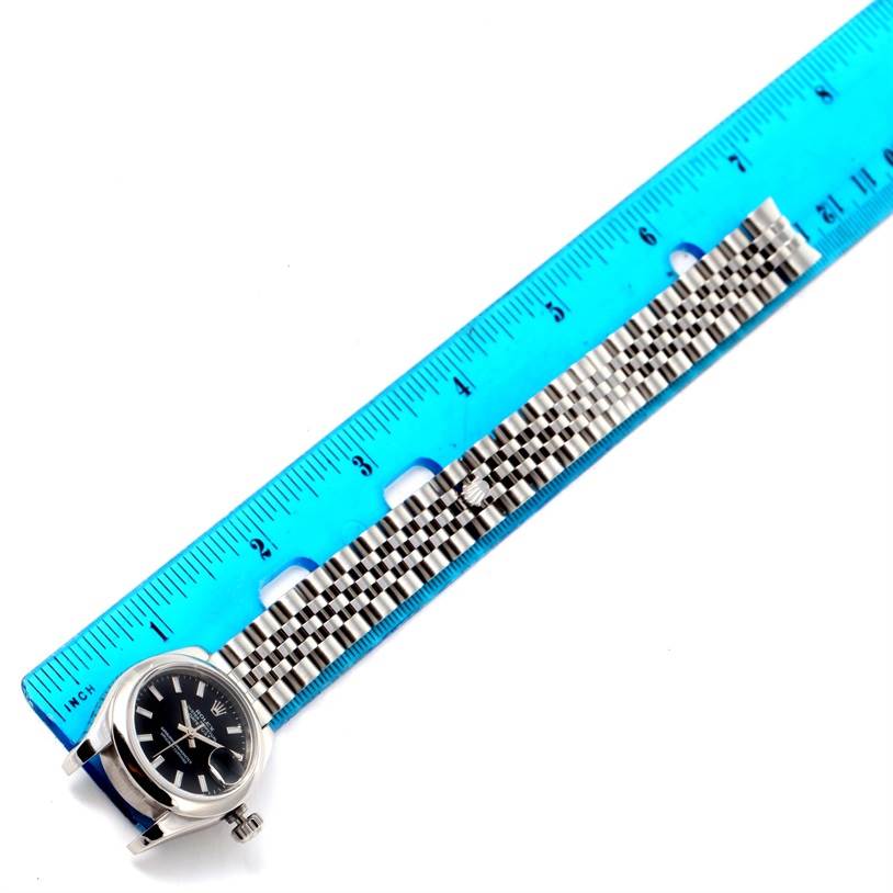 The image shows a Rolex Datejust 179160 Women
s Stainless Steel Black Dial 179160 Women
s Stainless Steel Black Dial watch with the face and partially extended bracelet next to a blue ruler for scale.