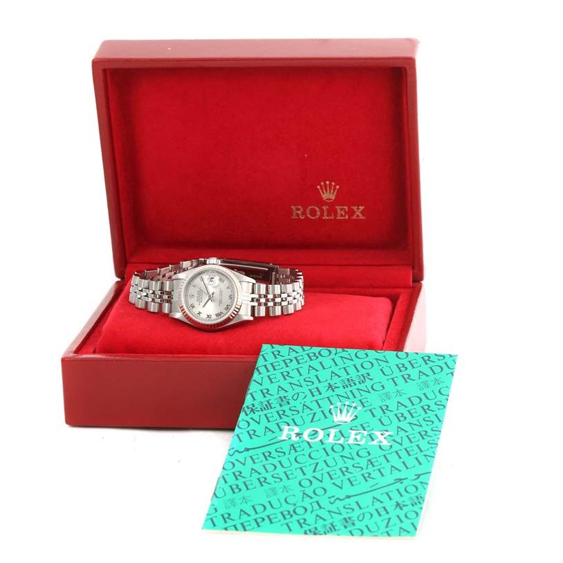 The Rolex Datejust 79174 Women
s Stainless Steel Silver Dial 79174 Women
s Stainless Steel Silver Dial watch is displayed in an open red box, showing the dial and bracelet, with a green booklet placed in front.