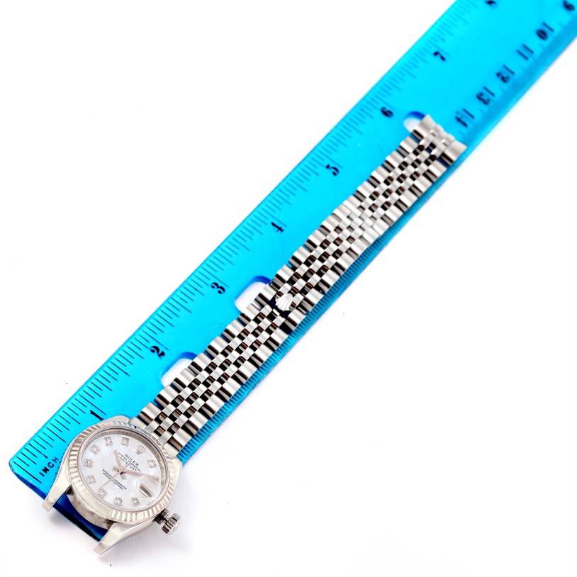 The Rolex Datejust 179174 Women
s Stainless Steel Mother of Pearl Dial 179174 Women
s Stainless Steel Mother of Pearl Dial watch is shown laid flat next to a blue ruler, displaying the watch face and bracelet.