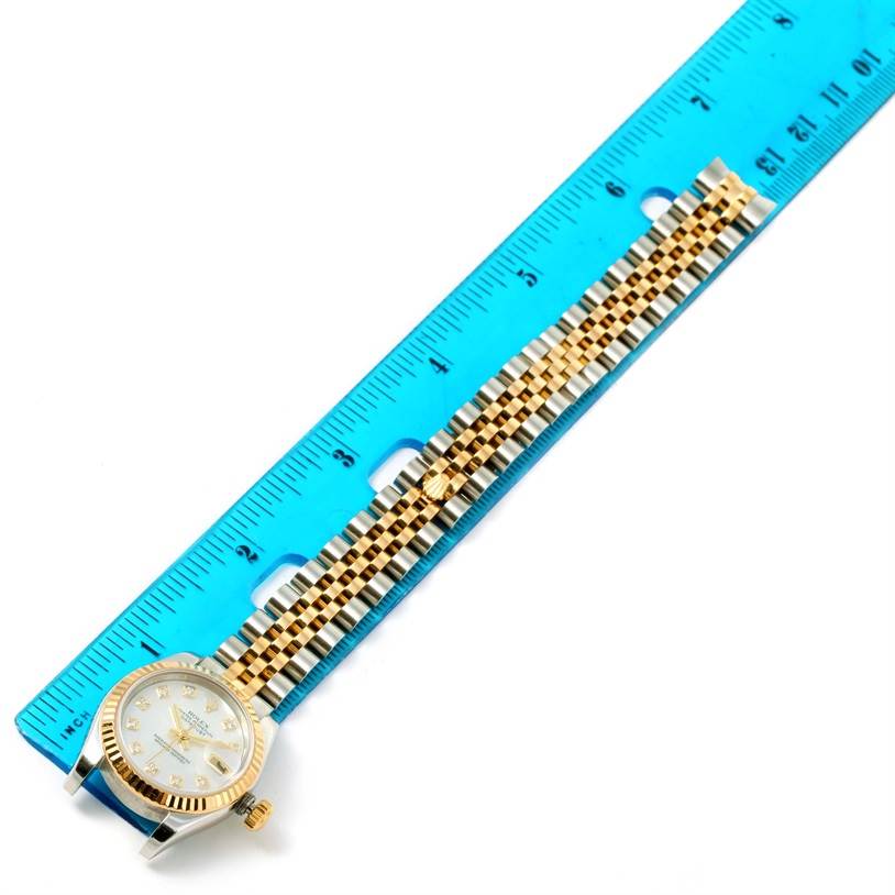 The Rolex Datejust 179173 Women's Steel and Gold (two tone) Mother of Pearl Dial 179173 Women's Steel and Gold (two tone) Mother of Pearl Dial is shown at a top-down angle, showing the face, bezel, crown, and bracelet, placed next to a ruler.