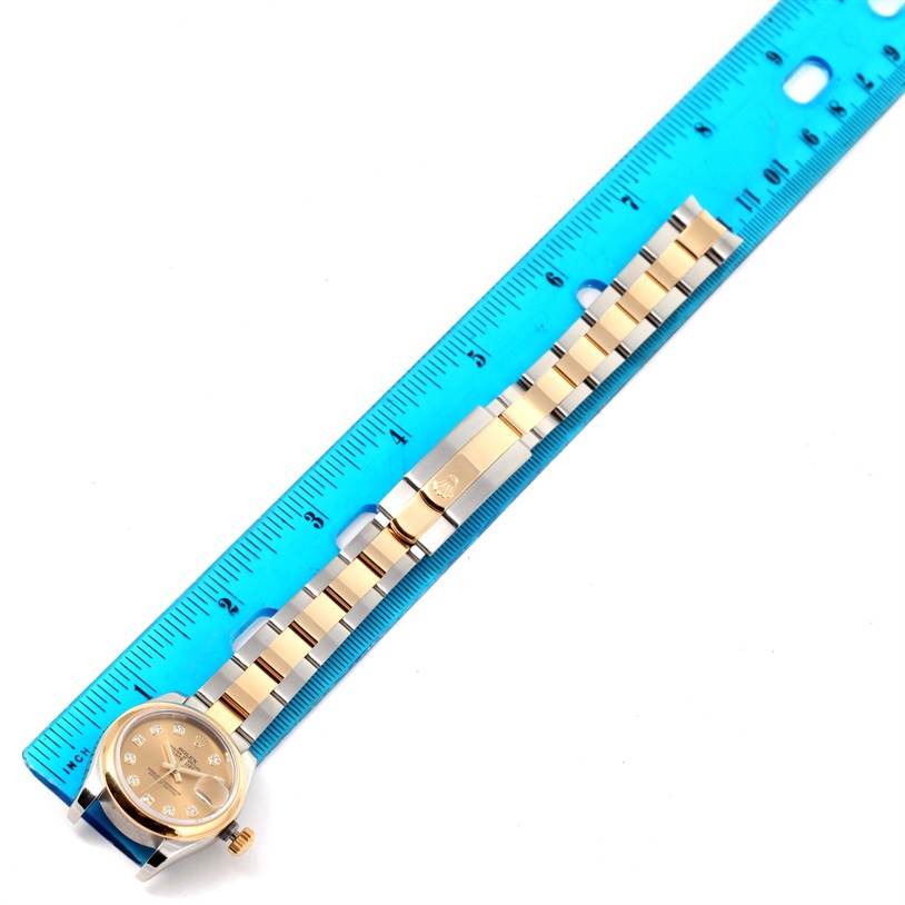 The image shows a Rolex Datejust 179163 Women's Steel and Gold (two tone) Champagne Dial 179163 Women's Steel and Gold (two tone) Champagne Dial watch laid flat next to a blue ruler, highlighting its bracelet and clasp.