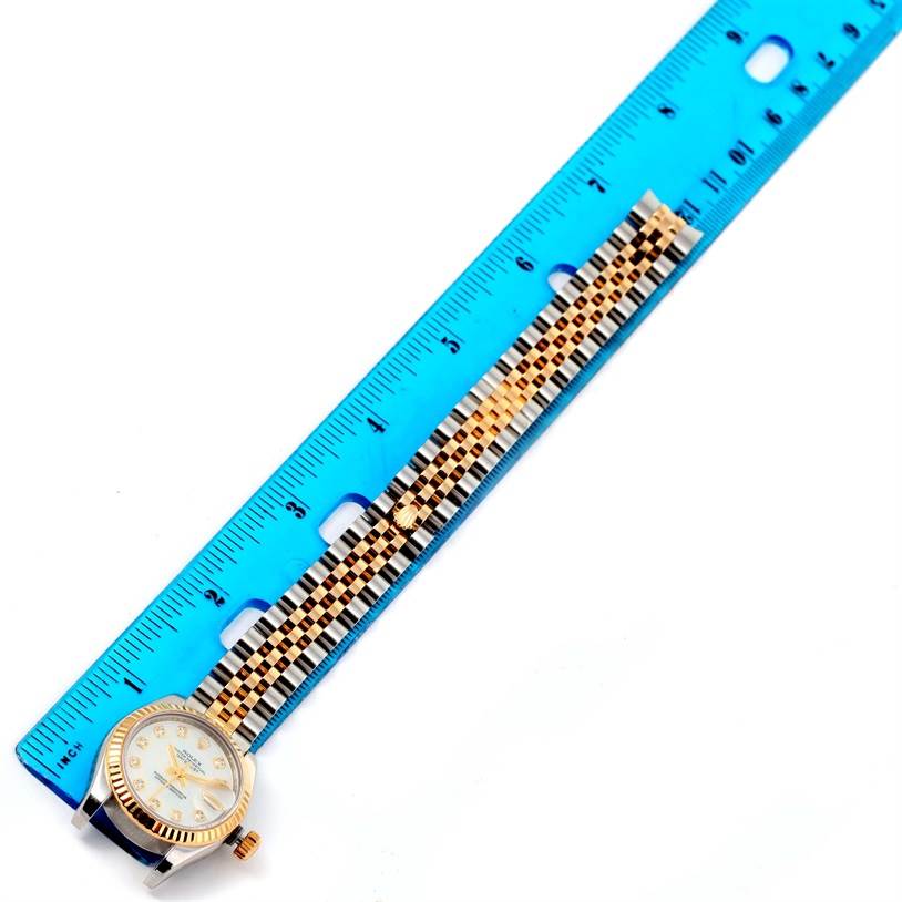 The Rolex Datejust 179173 Women's Steel and Gold (two tone) Mother of Pearl Dial 179173 Women's Steel and Gold (two tone) Mother of Pearl Dial watch is shown from above alongside a blue ruler, displaying its bracelet and face.