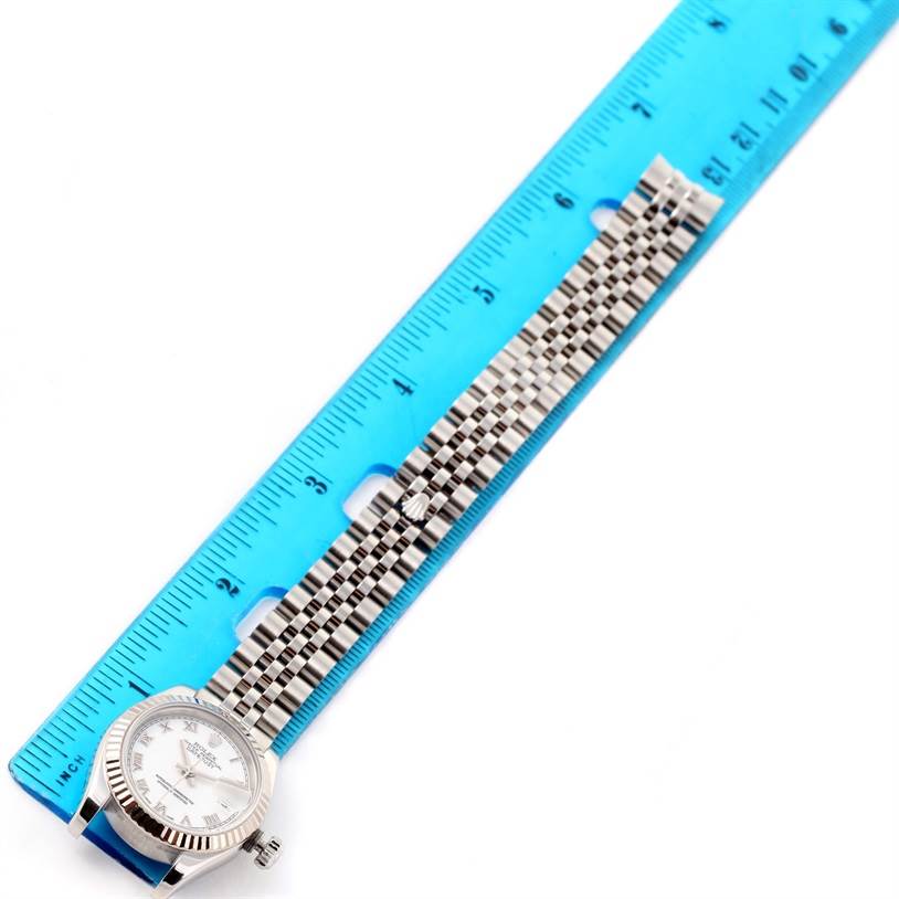 The image features a Rolex Datejust 179174 Women's Stainless Steel White Dial 179174 Women's Stainless Steel White Dial watch laid flat against a blue ruler, showing the face and bracelet.