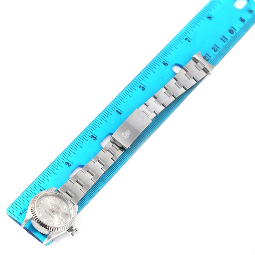 The Rolex Datejust 79174 Women's Stainless Steel Grey Dial 79174 Women's Stainless Steel Grey Dial watch is shown with a focus on its full bracelet and clasp, lying flat alongside a blue ruler.