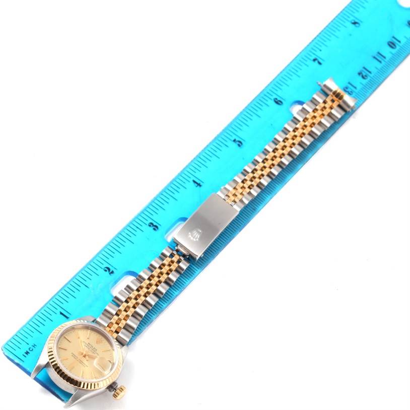 The image shows a Rolex Datejust 69173 Women
s Stainless Steel Champagne Dial 69173 Women
s Stainless Steel Champagne Dial watch lying flat on its dial side, with a ruler measuring its two-tone metal bracelet.