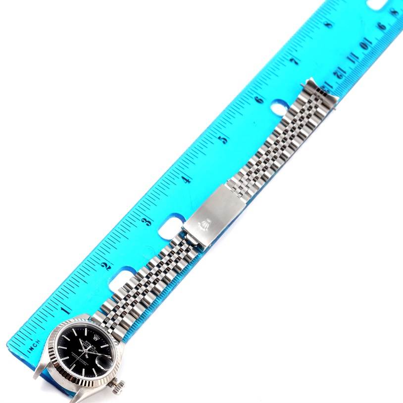 The Rolex Datejust 69174 Women's Stainless Steel Black Dial 69174 Women's Stainless Steel Black Dial watch is shown from a top-down angle, displaying the face, bracelet, and clasp near a ruler.