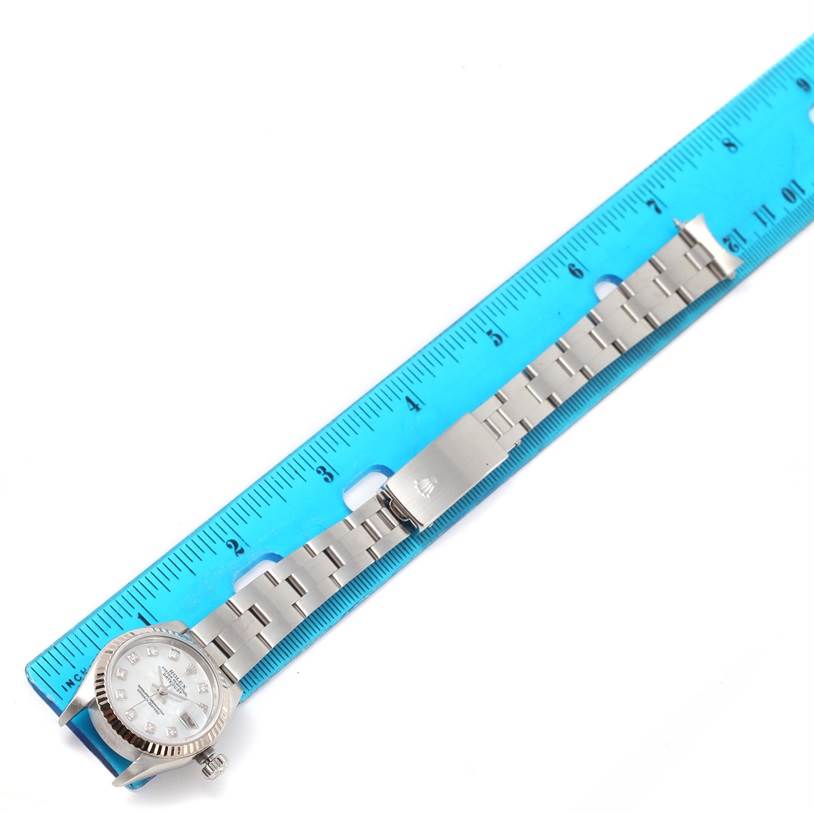 The Rolex Datejust 79174 Women's Stainless Steel Mother of Pearl Dial 79174 Women's Stainless Steel Mother of Pearl Dial watch is shown face-up with its bracelet fully extended next to a blue ruler.