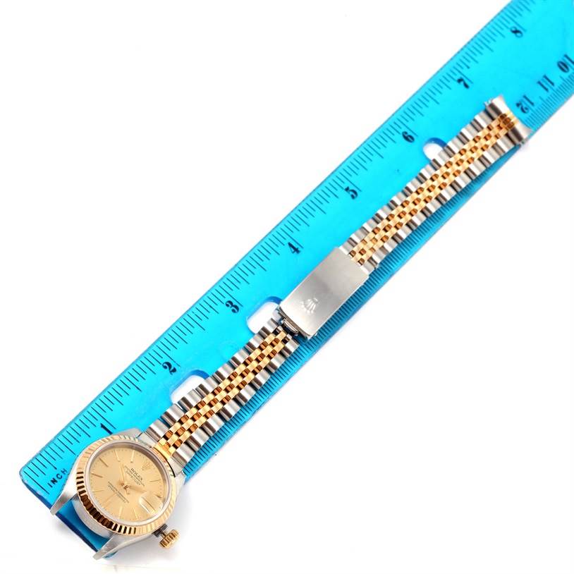 The image shows a Rolex Datejust 69173 Women
s Stainless Steel Champagne Dial 69173 Women
s Stainless Steel Champagne Dial watch and its metal bracelet lying flat next to a blue ruler for scale.