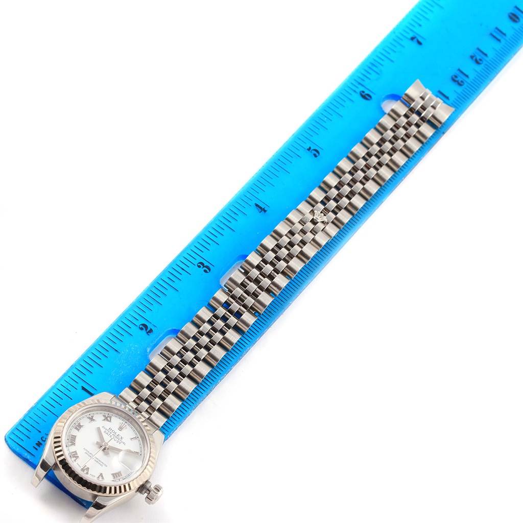 The Rolex Datejust 179174 Women
s Stainless Steel White Dial 179174 Women
s Stainless Steel White Dial watch is shown from a top-down angle alongside a blue ruler, displaying the face and bracelet.