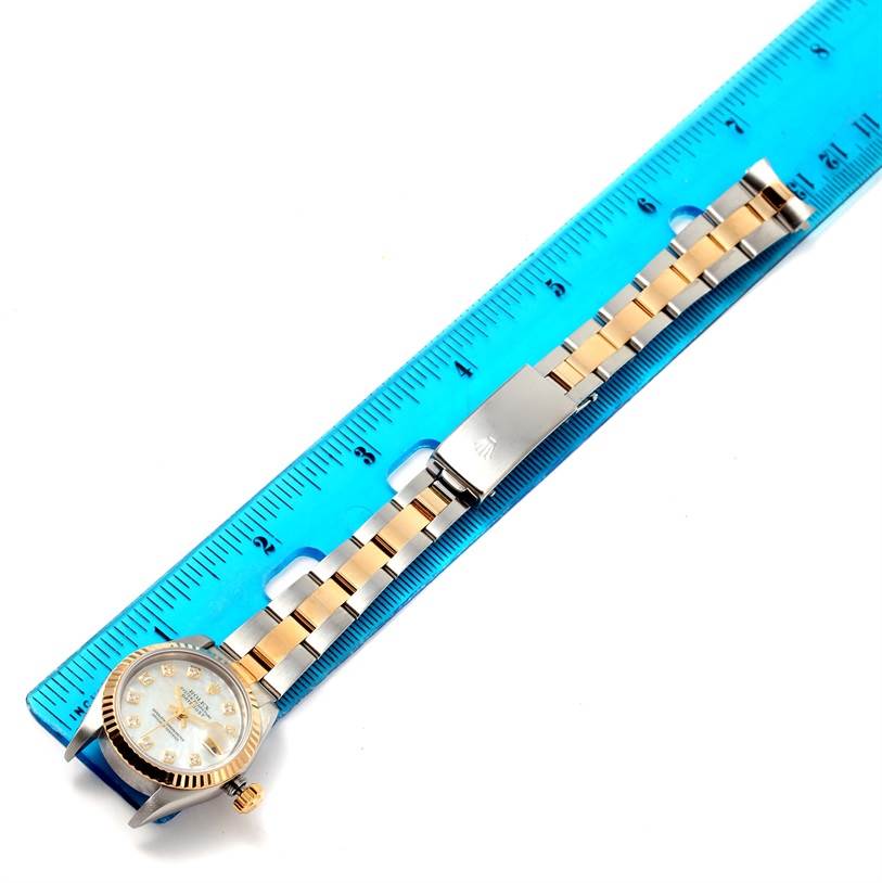 The Rolex Datejust 79173 Women
s Stainless Steel Mother of Pearl Dial 79173 Women
s Stainless Steel Mother of Pearl Dial watch is shown from a top-down angle, displaying its face, bracelet, and clasp, alongside a ruler for scale.