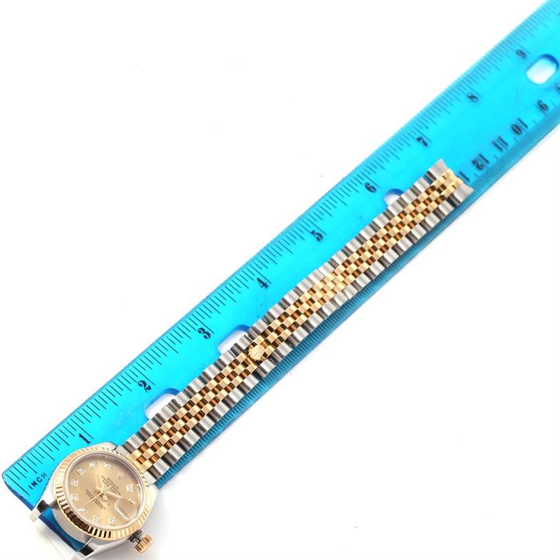 The Rolex Datejust 179173 Women's Steel and Gold (two tone) Champagne Dial 179173 Women's Steel and Gold (two tone) Champagne Dial watch is shown flat, with the face and bracelet alongside a blue ruler for measurement.