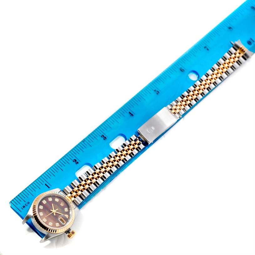 The Rolex Datejust 79173 Women's Steel and Gold (two tone) Mother of Pearl Dial 79173 Women's Steel and Gold (two tone) Mother of Pearl Dial watch is shown from a top-down angle alongside a ruler, highlighting its bracelet and face.