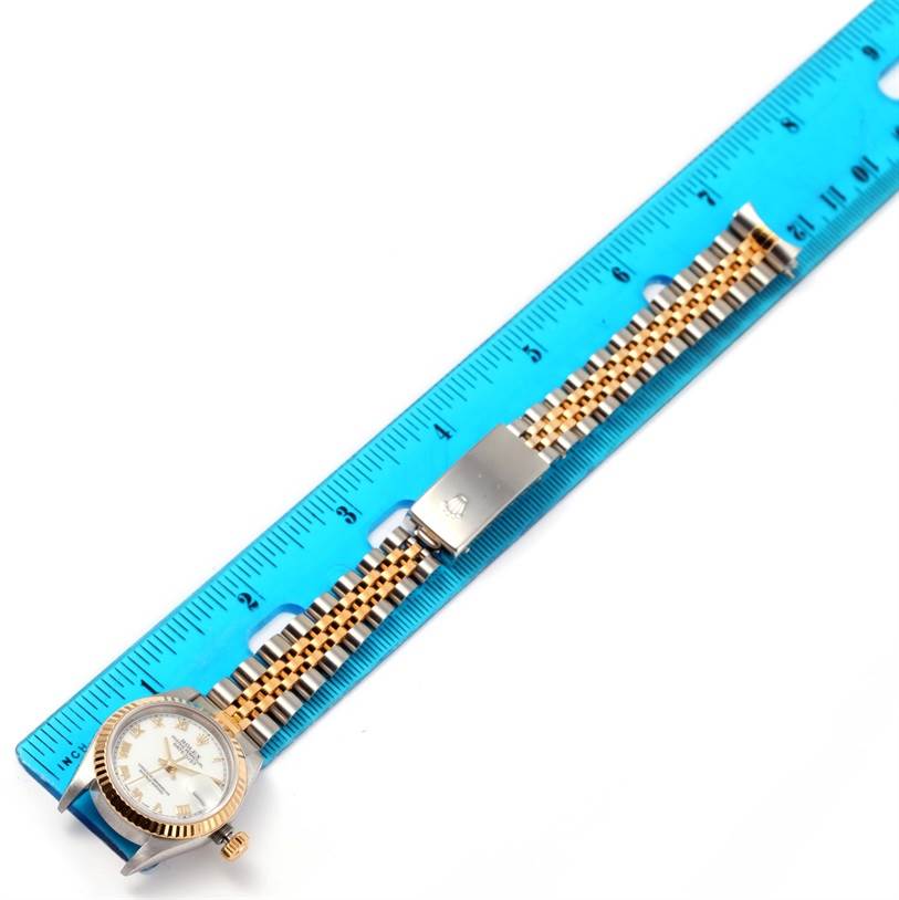 The Rolex Datejust 79173 Women
s Stainless Steel White Dial 79173 Women
s Stainless Steel White Dial watch is shown from a top-down angle, with a focus on the dial, bracelet, and clasp against a blue ruler.