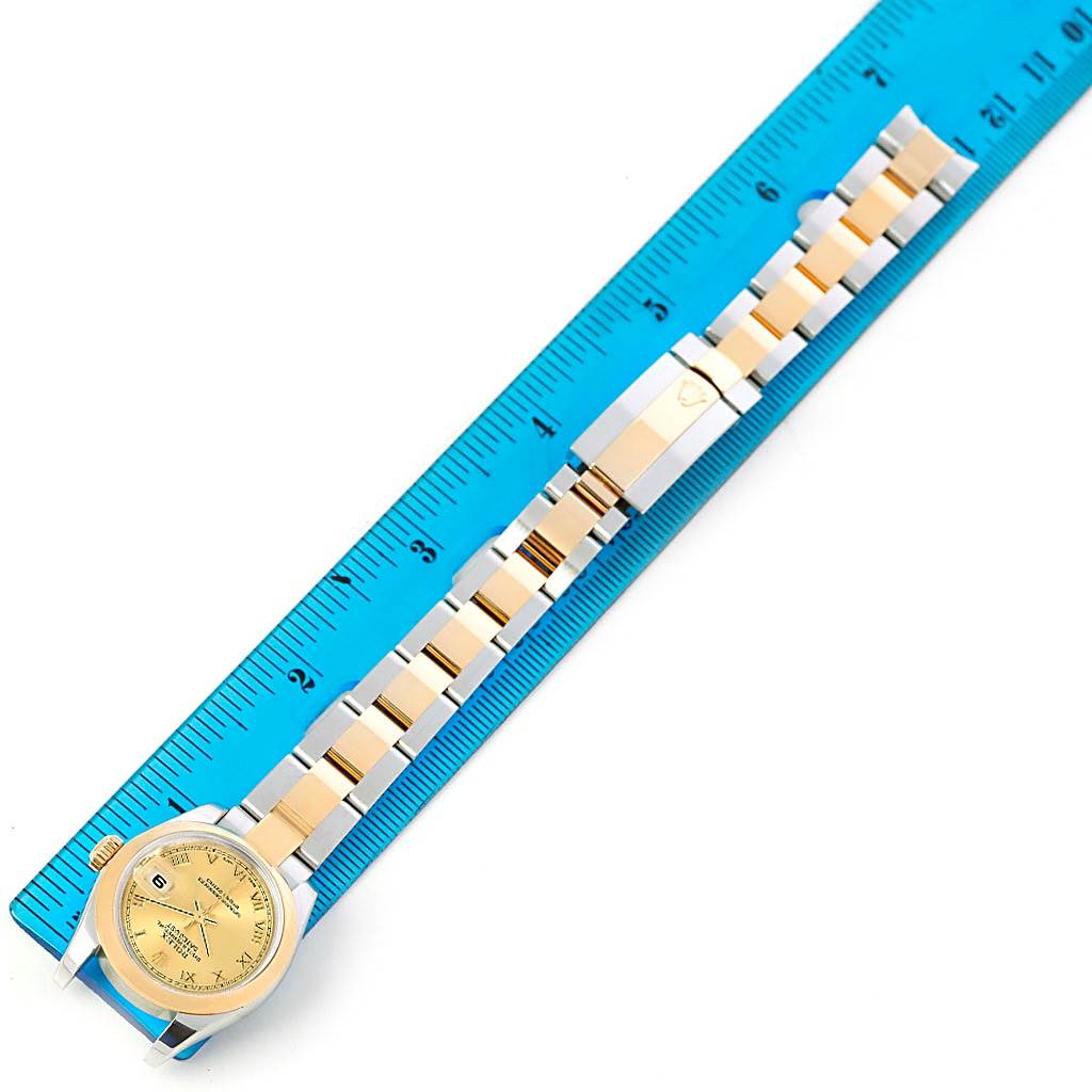 The image shows a Rolex Datejust 179163 Women's Steel and Gold (two tone) Champagne Dial 179163 Women's Steel and Gold (two tone) Champagne Dial watch, including its gold dial, bezel, and two-tone bracelet, laid next to a blue ruler.