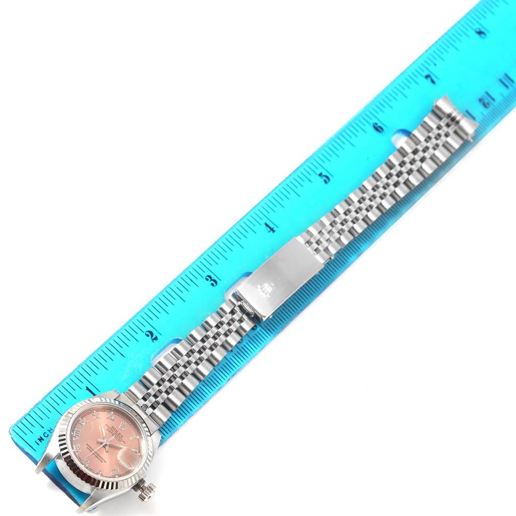 The image shows a Rolex Datejust 69174 Women
s Stainless Steel Pink Dial 69174 Women
s Stainless Steel Pink Dial watch laid flat next to a blue ruler, highlighting the face, bezel, and band.